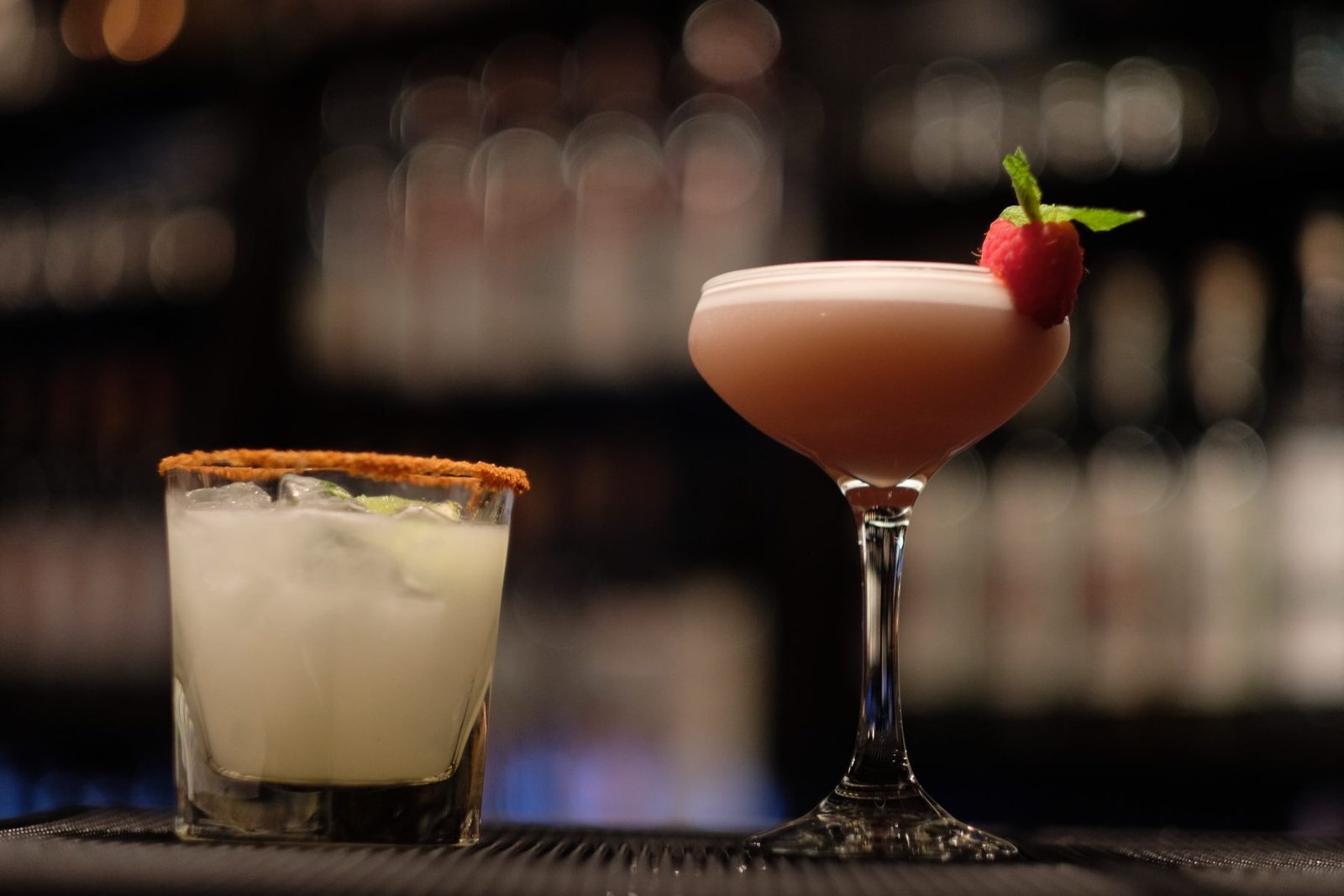 A pair of cocktails set against the warm-lit back bar
